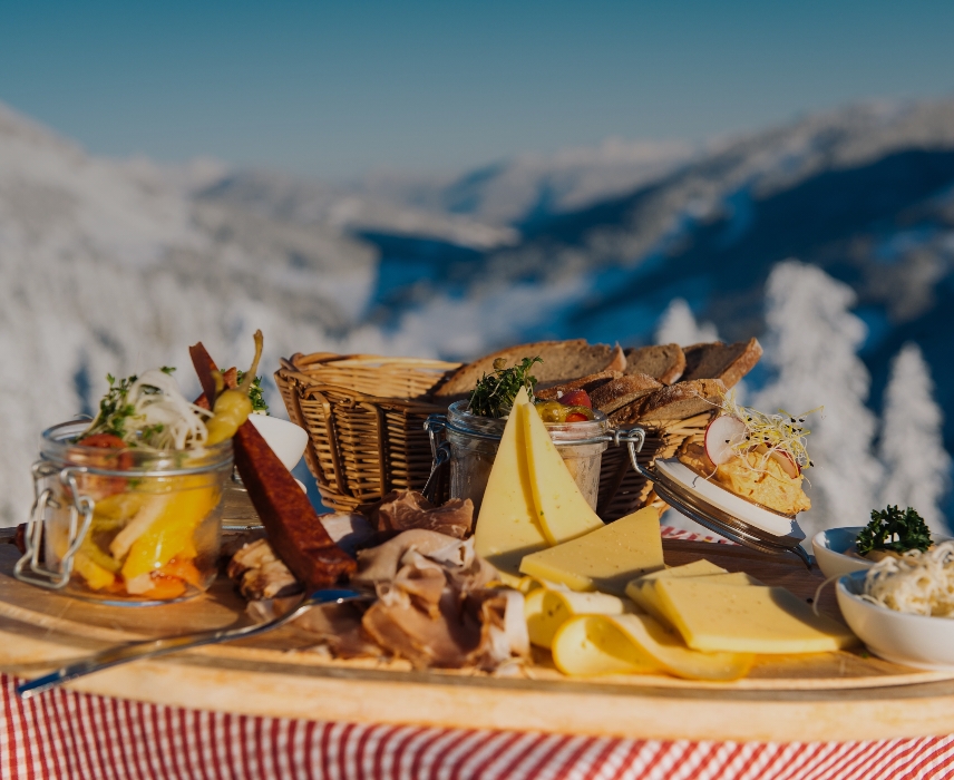 Cheese, bread and sausages on a wooden plate in the mountains
